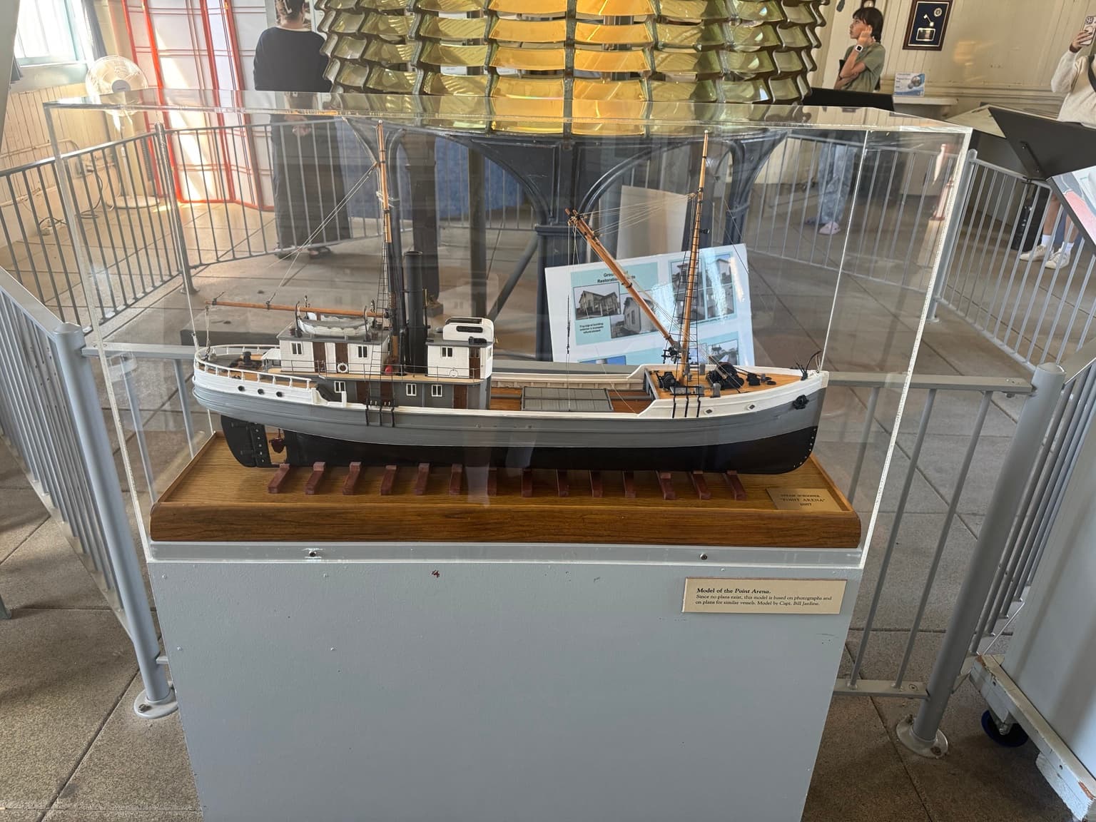 The mounted Pigeon Point Fresnel lens behind a glass case containing a model of the steam schooner Point Arena