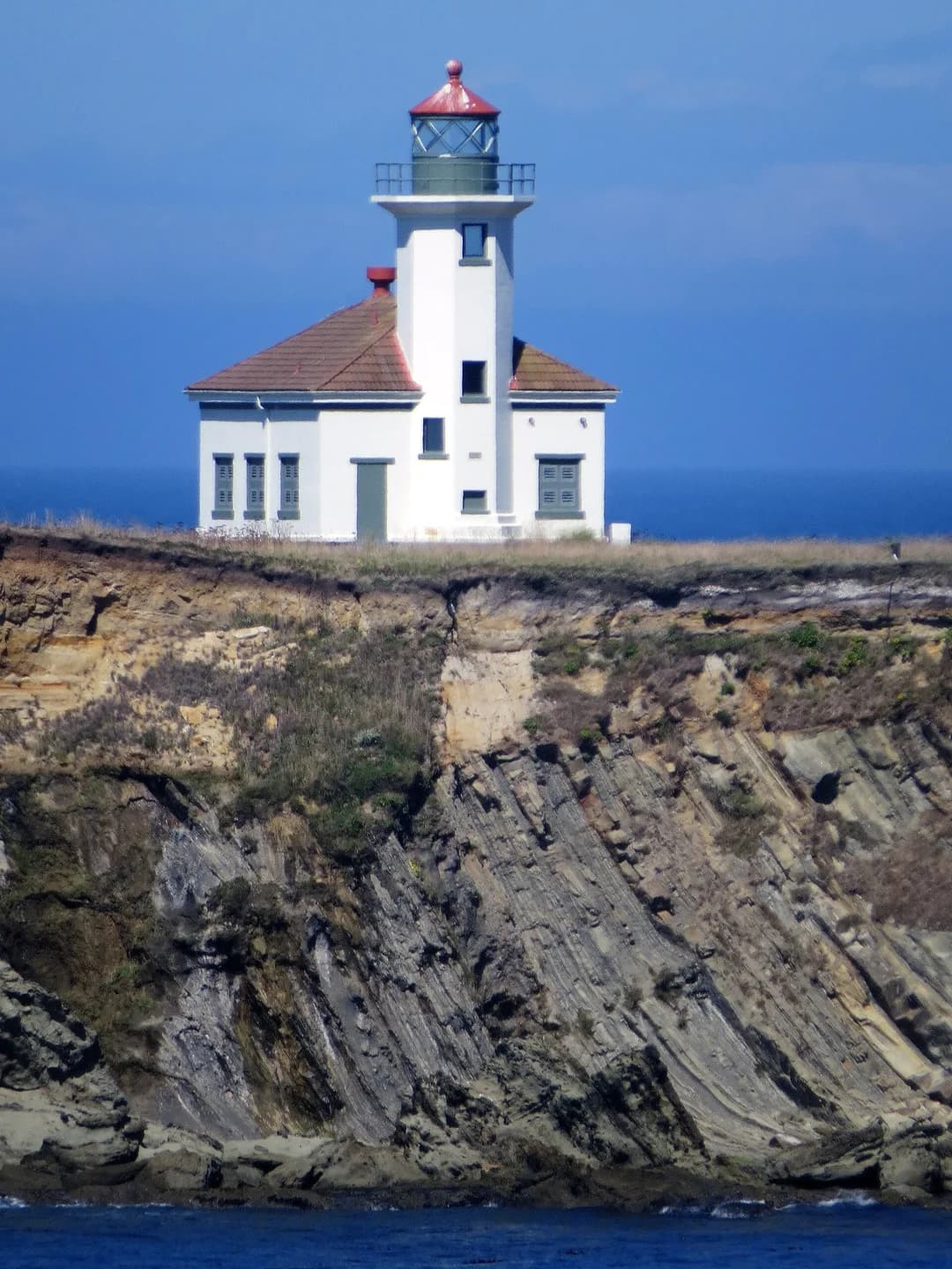 White Cape Arago lighthouse tower and attached building above a rocky shoreline.