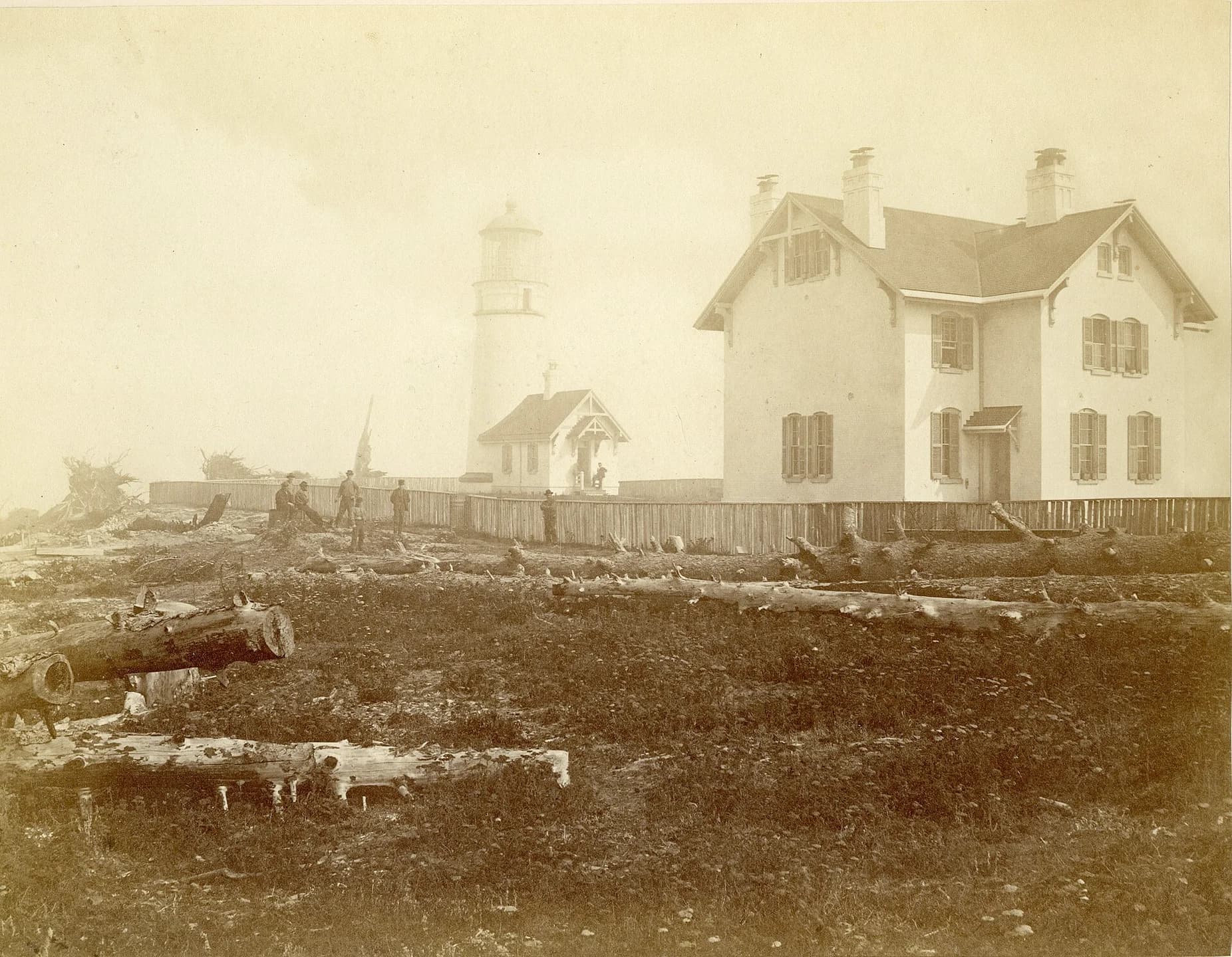 Nineteenth-century photograph of a lighthouse tower and wooden station buildings on a bare headland.