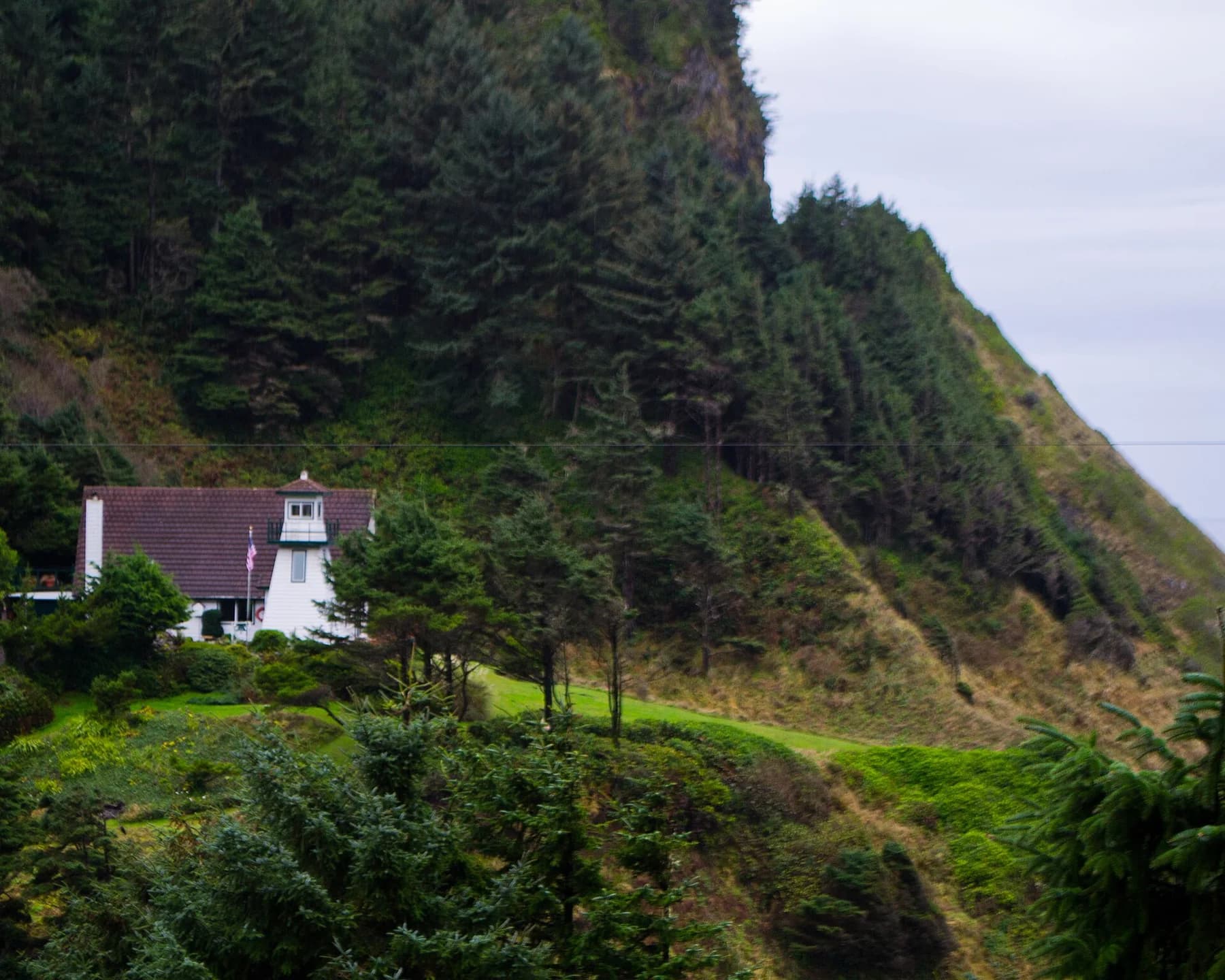 Small white lighthouse and residence partly hidden by trees on a wooded hillside.