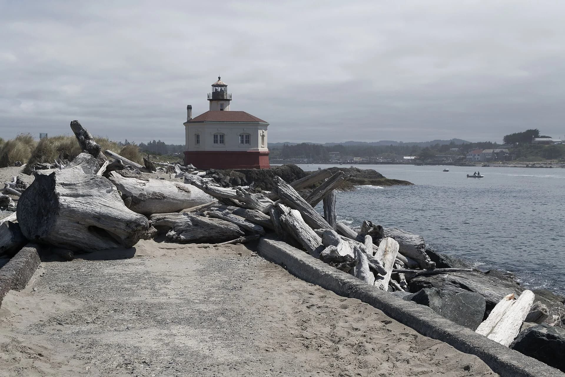 Driftwood and rocks in the foreground of the Coquille River Lighthouse beside the water.