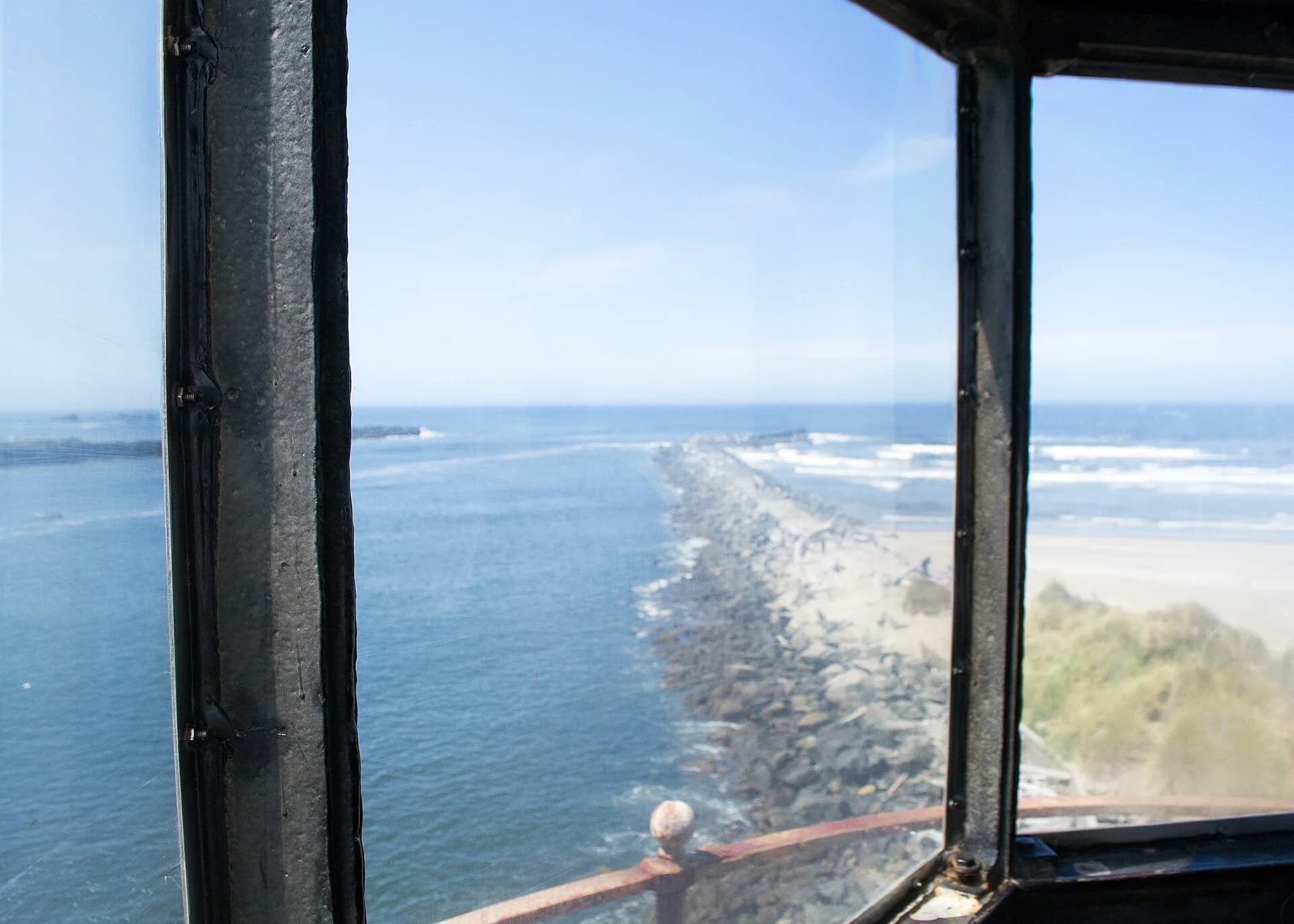 View through a lighthouse window along a rock jetty toward the ocean.