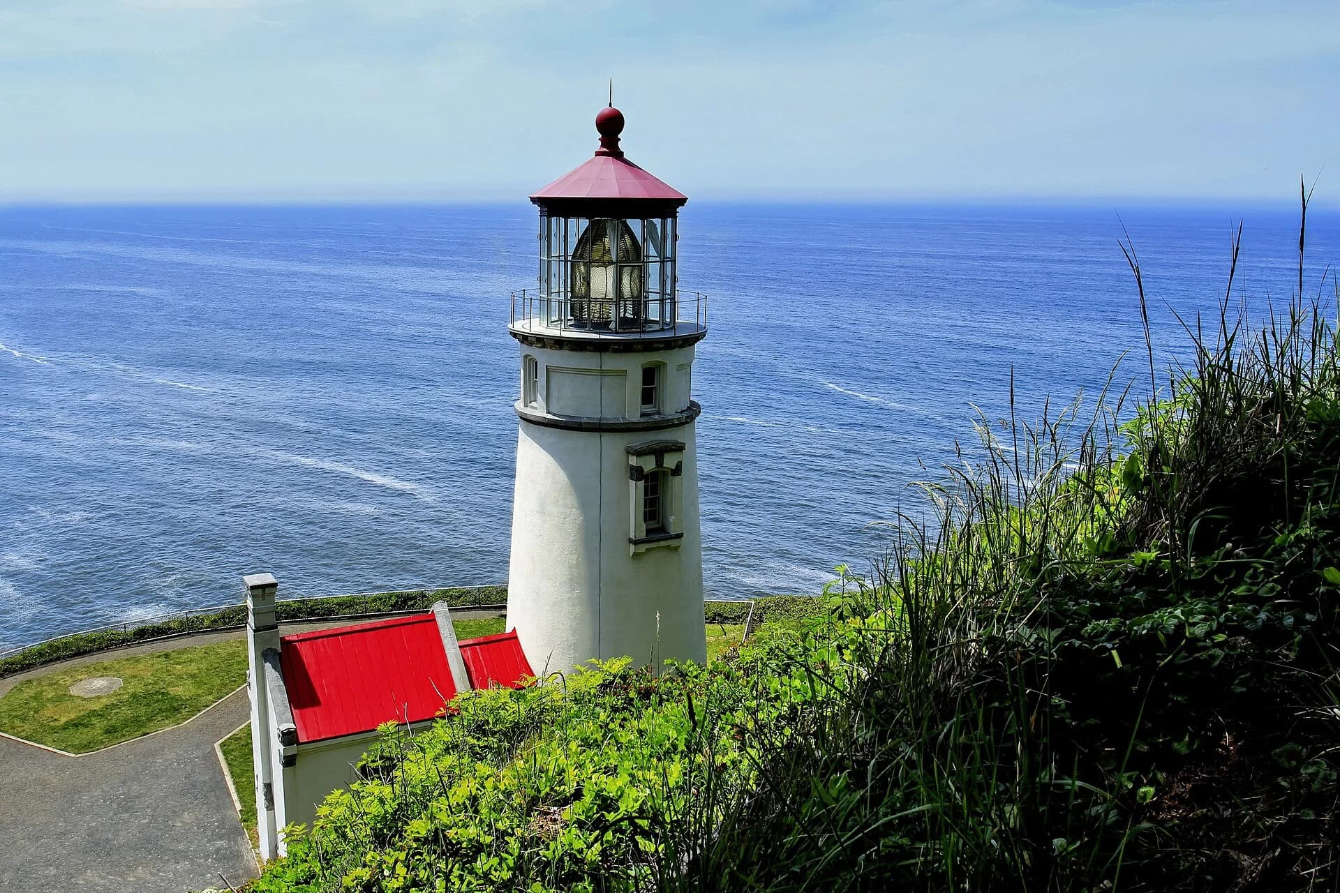 White lighthouse tower with red lantern roof on the grassy Heceta Head promontory above the Pacific.