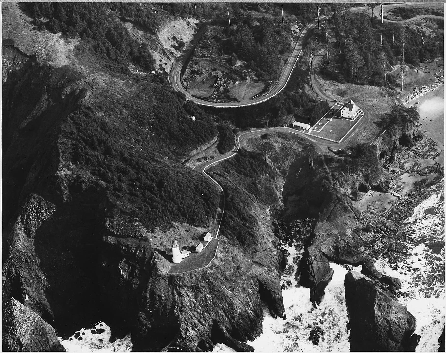 Historic aerial view of the Heceta Head tower, station buildings and wooded headland.