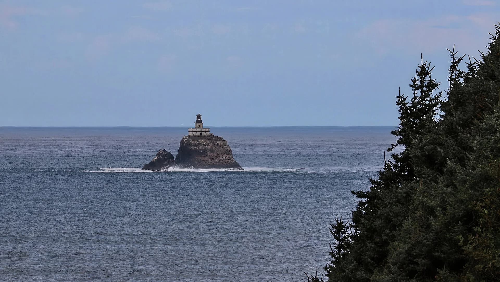 Tillamook Rock Lighthouse on an offshore rock, with trees framing the distant view.
