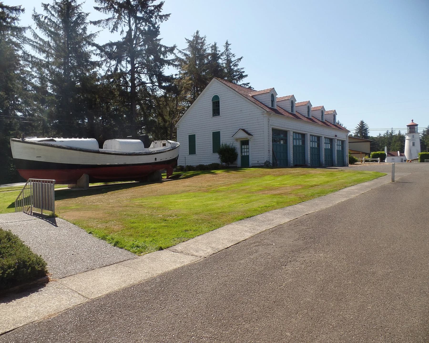 Display lifeboat beside a white museum building, with the lighthouse in the background.
