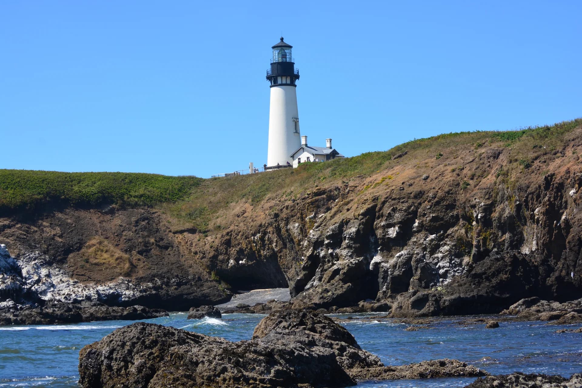 Tall white lighthouse tower on a basalt headland seen from the rocky Cobble Beach below, Yaquina Head, Oregon.
