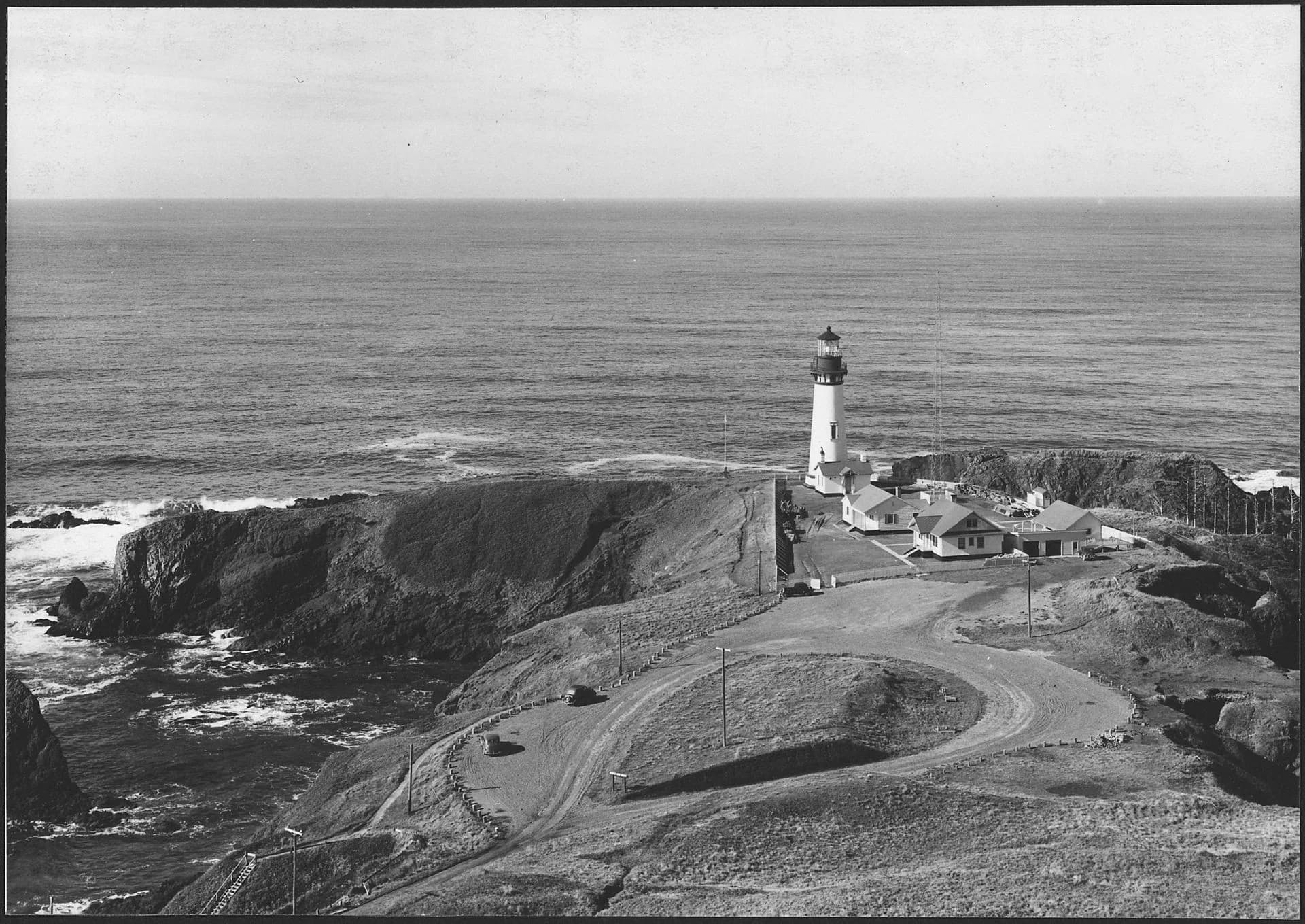 Black-and-white 1938 photograph of Yaquina Head Lighthouse with its keeper dwellings on the headland.